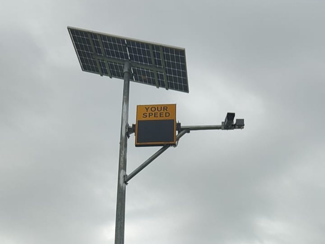Complete off-grid installation on a rural highway: solar panel, radar speed display, ANPR camera and battery cabinet on a single pole